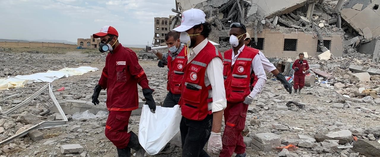 Fem hjelpearbeidere fra Røde Kors bærer en død kropp innpakket i plast