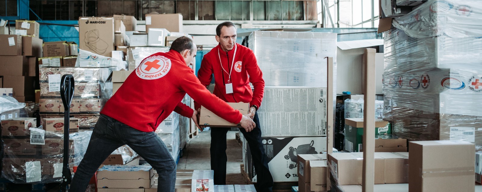 To frivillige fra Røde Kors lemper esker med nødhjelp på et lager.