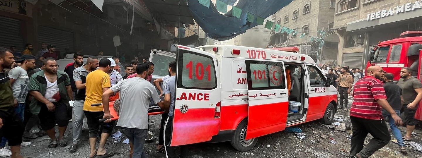 I en utbombet gate bærer frivillige og sivile en person på båre inn i en ambulanse.