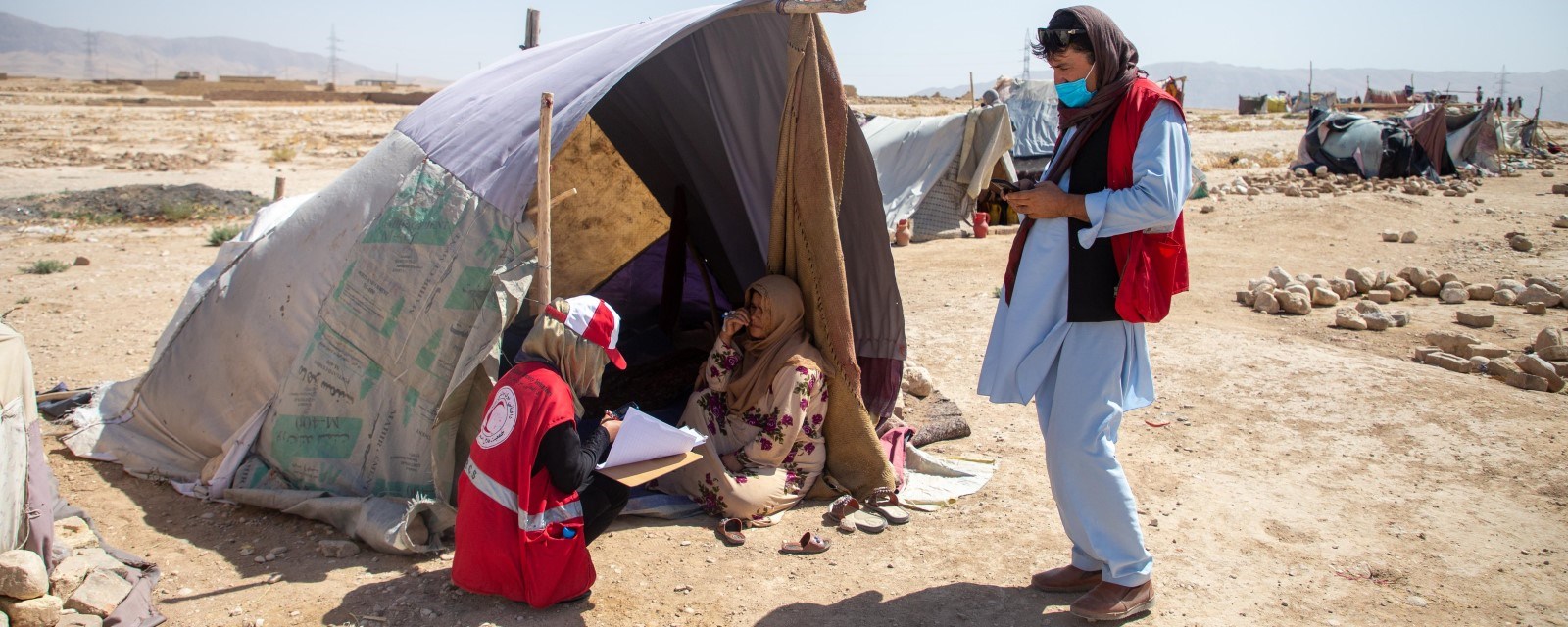 To personer fra Røde Kors snakker med en kvinne som sitter i et provisorisk telt. 