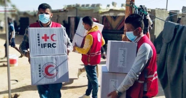 To menn med munnbind og vest fra Røde Halvmåne bærer esker med logoen til  IFRC på