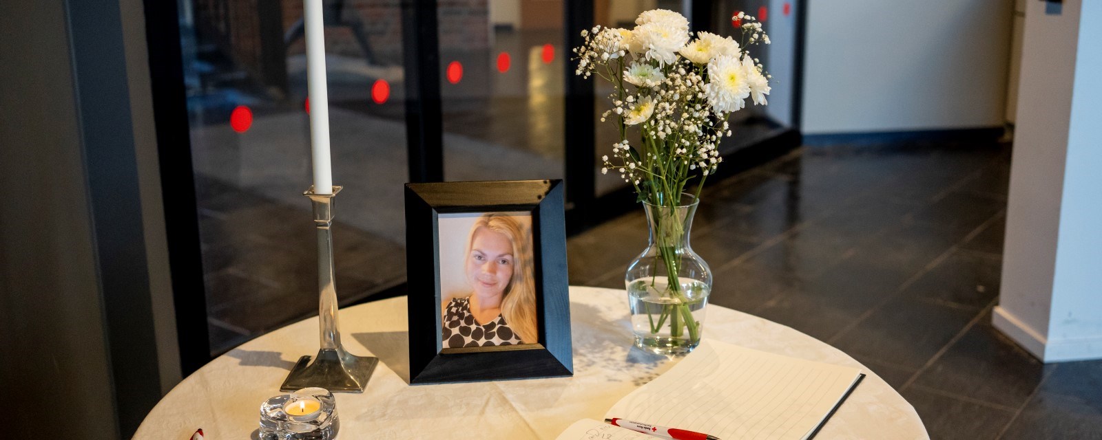 Et bord med blomster, stearinlys og et bilde av Karoline står i resepsjonen ved inngangen til Røde Kors. 