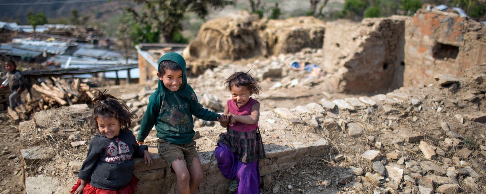 Tre barn sitter ved ruinene av et jordskjelvrammet, ødelagt hus