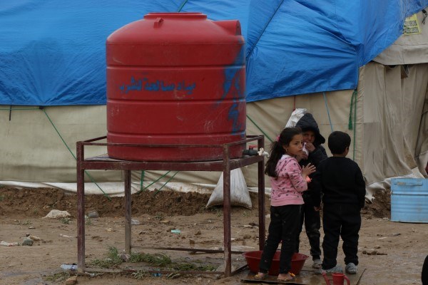 Tre små barn står ved en vanntank.