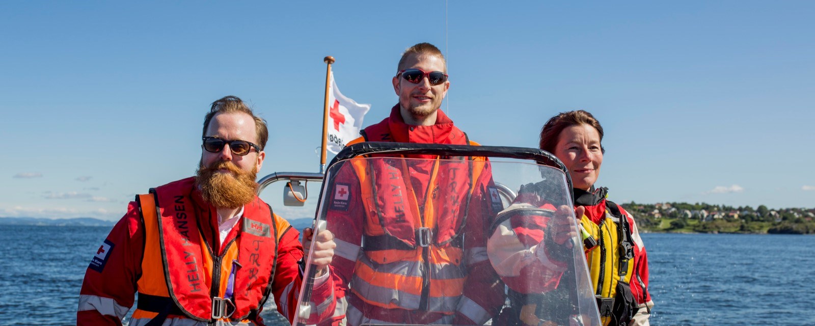 Tre hjelpekorpsere til sjøs med vind i skjegget, uniformer og - selvfølgelig - redningsvest.