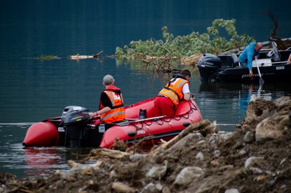 To personer kjører en gummibåt langs vannkanten og kikker ned i vannet.