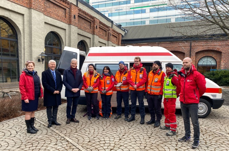 Ti personer står foran en Røde Kors-ambulanse.