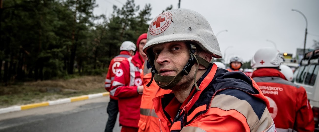 En mann med Røde Kors-hjelm står ute og har skitt på hjelmen og i ansiktet.