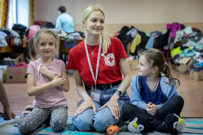 En kvinne fra Røde Kors sitter på gulvet med et barn på hver side.