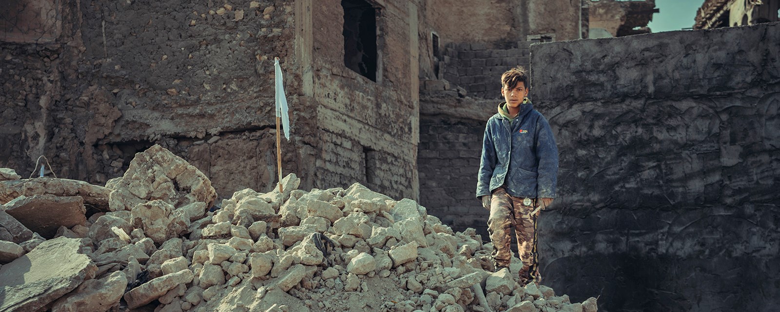 En gutt står i ruinene av et utbombet hus