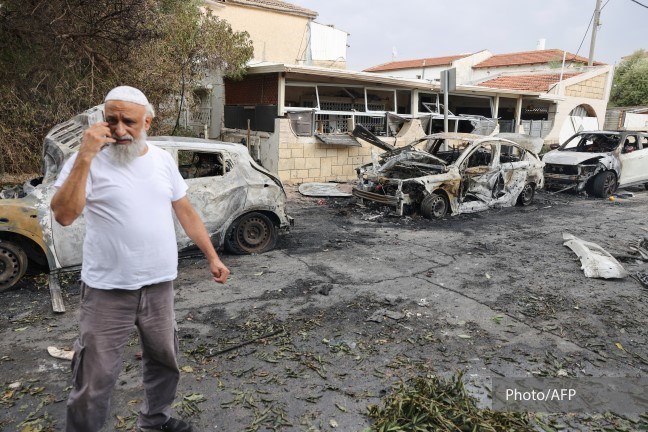 En eldre mann står fortvilet foran en utbombet bygning og biler