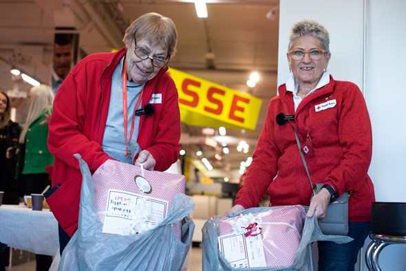 Frivillige i Røde Kors viser frem julegaver de har pakket inn før jul. De holder to store poser i hendene fulle av gaver.
