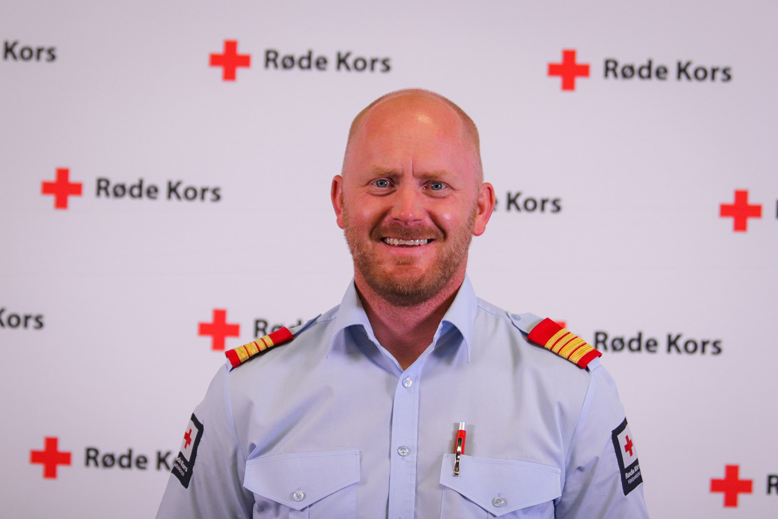 Portrett av en mann i hjelpekorpsuniform med røde-kors-bakgrunn