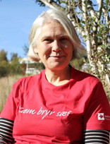 Kari Lydersen sitter på en benk og ser mot kameraet og smiler, i en rød tskjorte med påskriften "Kæm bryr sæ?". 