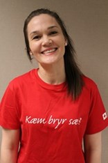 Maria Birkely ser mot kameraet og smiler, i en rød tskjorte med påskriften "Kæm bryr sæ?". Foto.