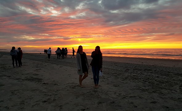 Silhuetter av to jenter på strand i solnedgang.