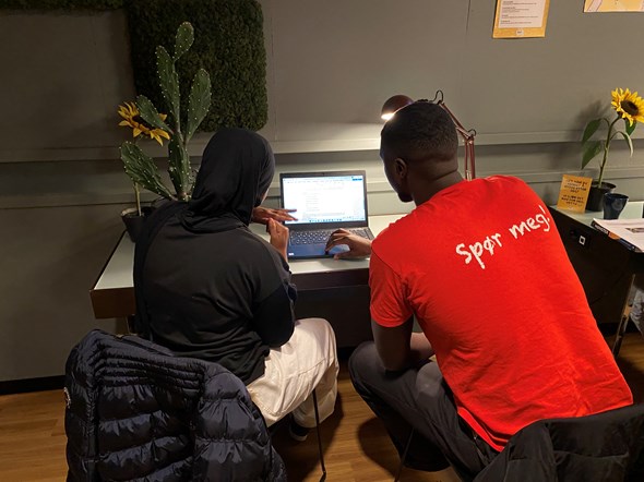 En mann hjelper en ungdom med leksene ved en datamaskin