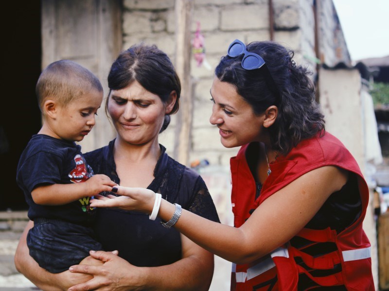 En kvinne fra Røde Kors hilser på en ung mor som holde en baby i armene
