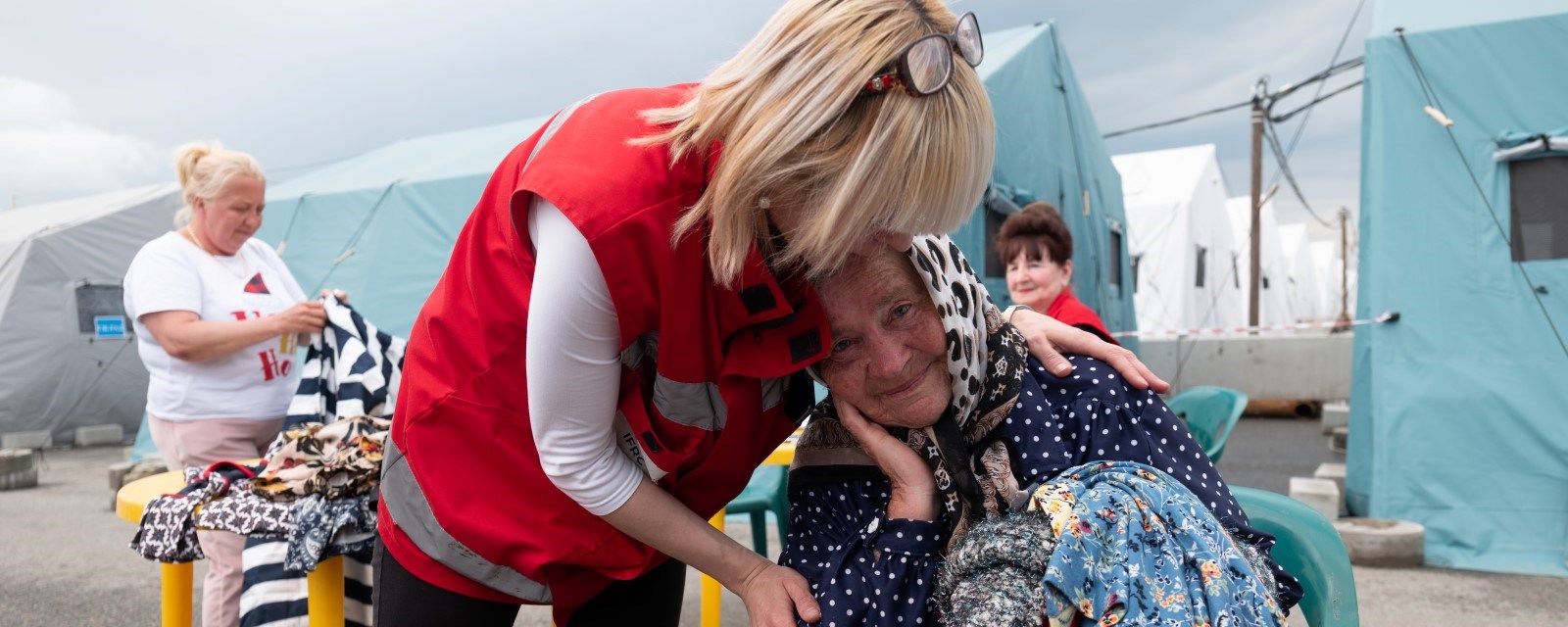 En kvinne fra Røde Kors holder rundt en eldre kvinne som sitter på en stol.