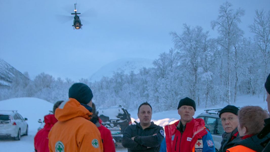 En gruppe med frivillige fra redningstjenster får ros av Røde Kors presienten Robert Mood i det et helikopter farer over dem