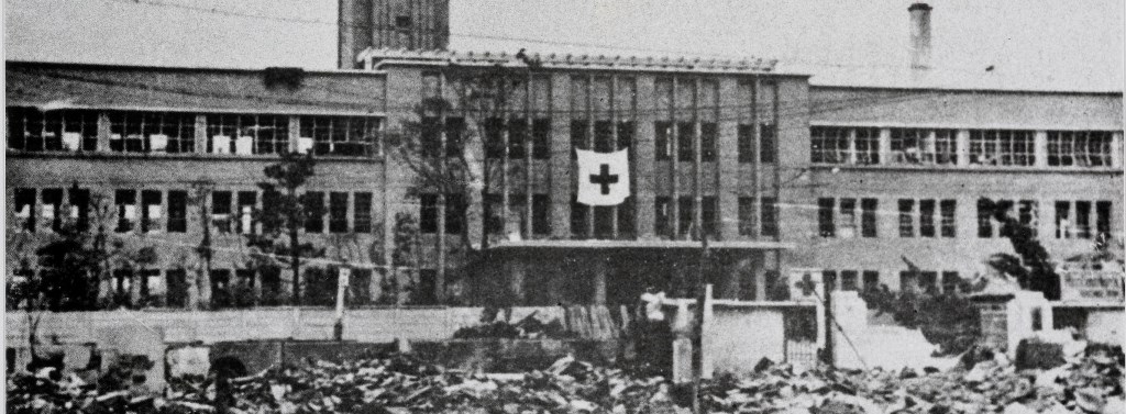 Svart hvitt bilde av et sykehus med det røde kors, omringet av bygninger i ruiner
