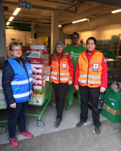 Tre personer fra Røde Kors i Røde Kors vester som henter matvarer fra Kiwi. Man ser en Kiwi ansatt og matvarene som blir hentet.