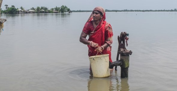 En kvinne henter vann fra en pumpe som står i vannet.