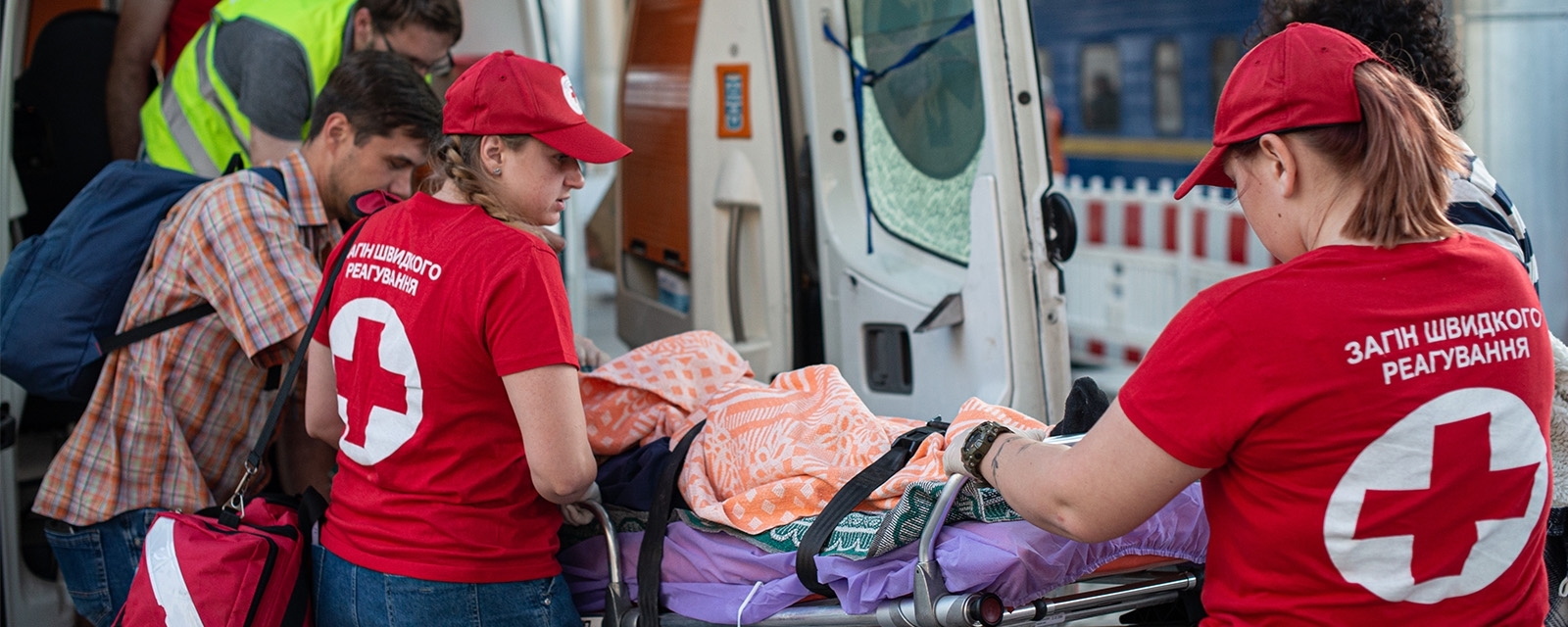 En person blir trillet ut fra en ambulanse av to røde kors frivillige