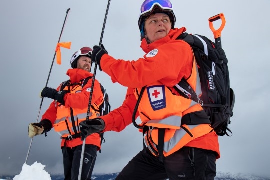 To frivillige fra Hjelpekorpset stikker lange pinner ned i snøen for å søke etter personer som er tatt av skred under en øvelse.