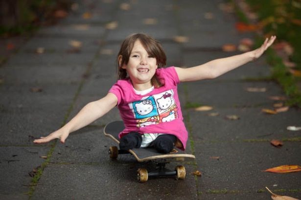 En smilende jente, 11 år, sitter på et rullebrett og balanserer med armene.