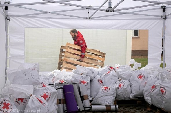Bak en haug med store Røde Kors-poser bærer en mannlig frivillig to paller