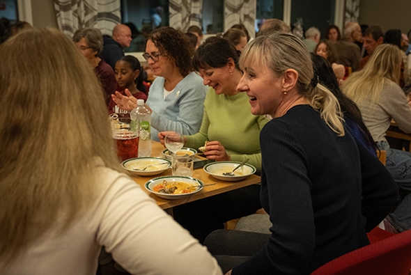 Folk sit rundt eit bord og pratar og ler.