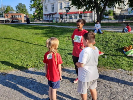 En frivillig står og prater med to barn i BARK-aktivitet ute i en park
