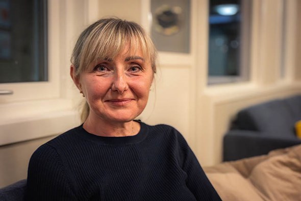 Kvinne smiler til kamera. Ho sit i ein sofa.