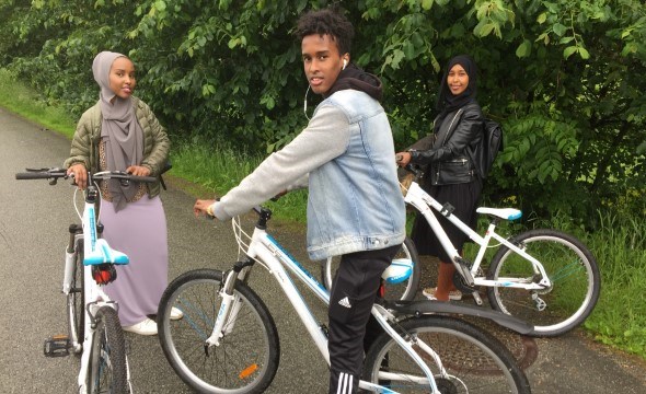 En gutt og to jenter som holder hver sin sykkel.