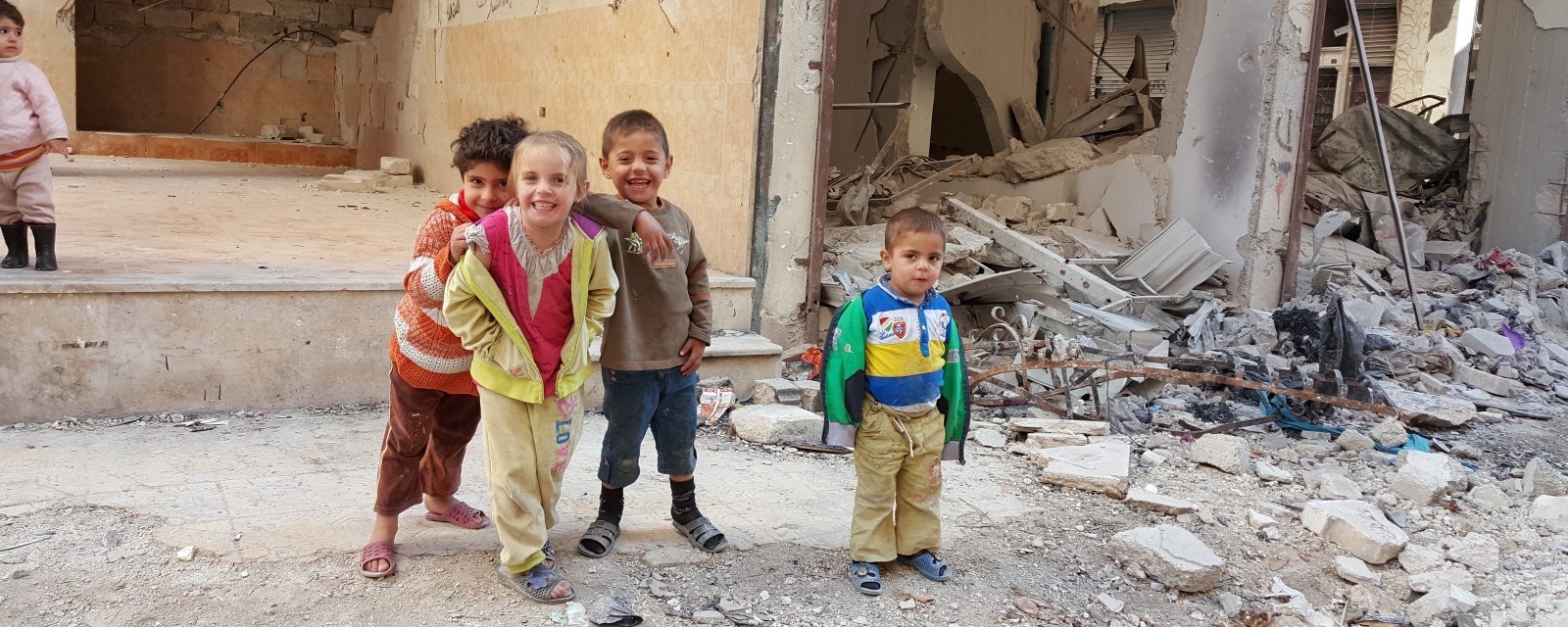 Barn står i en gate omgitt av ruiner