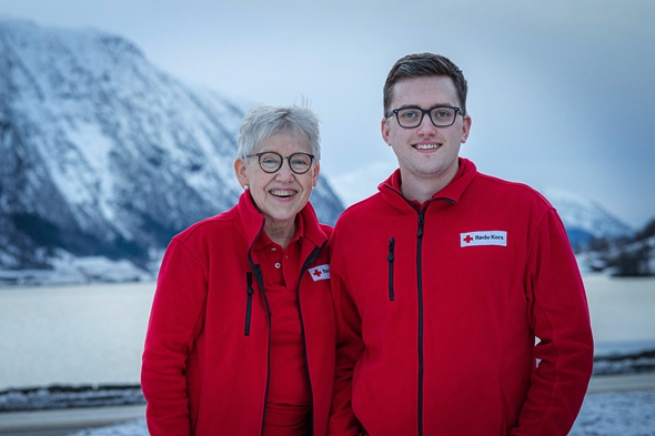 Dame og mann i røde jakker framfor fjell