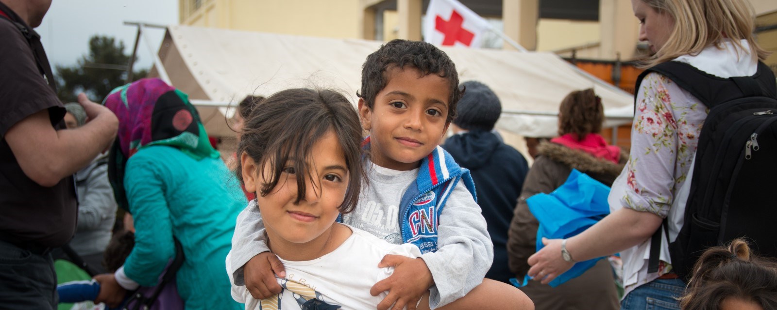 En ung jente bærer en enda yngre gutt på ryggen i Diavata Camp, en flyktningleir i Hellas. Foto: Thomas Andre Syvertsen/Norges Røde Kors