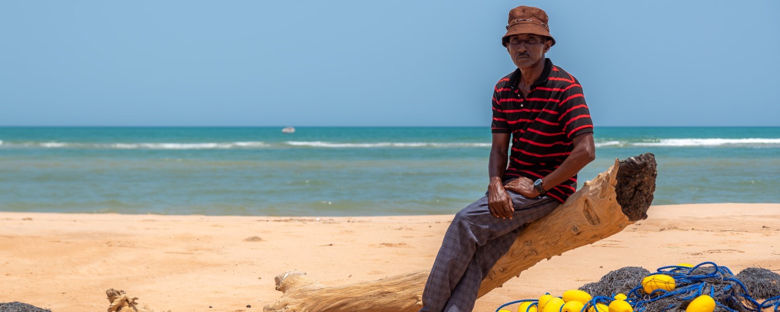 En mann sitter på en tømmerstokk på stranden