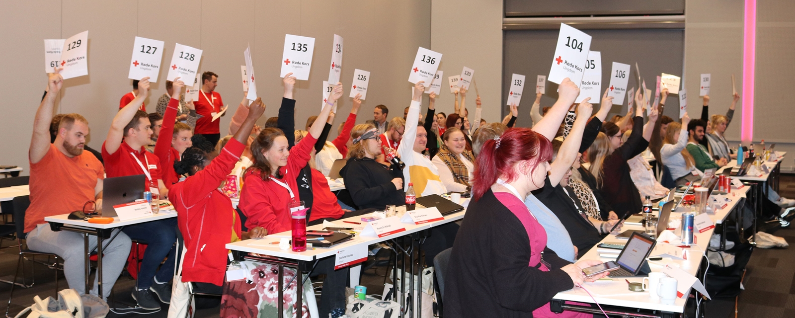 Ungdomer på årsmøte i Røde Kors Ungdom som rekker sine delegasjonsskilt i været 
