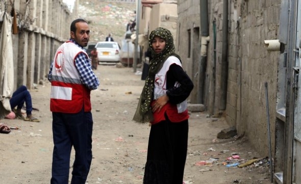 En mann og en kvinne med vester fra Jemen Røde Halvmåne går bortover en gate samtidig som de kikker seg tilbake.