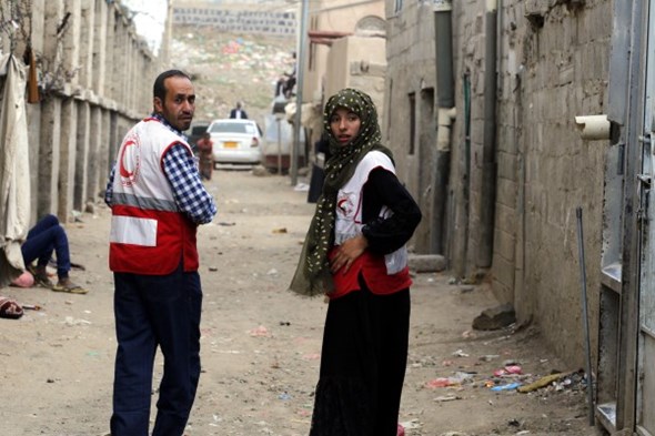 En mann og en kvinne med vester fra Jemen Røde Halvmåne går bortover en gate samtidig som de kikker seg tilbake.