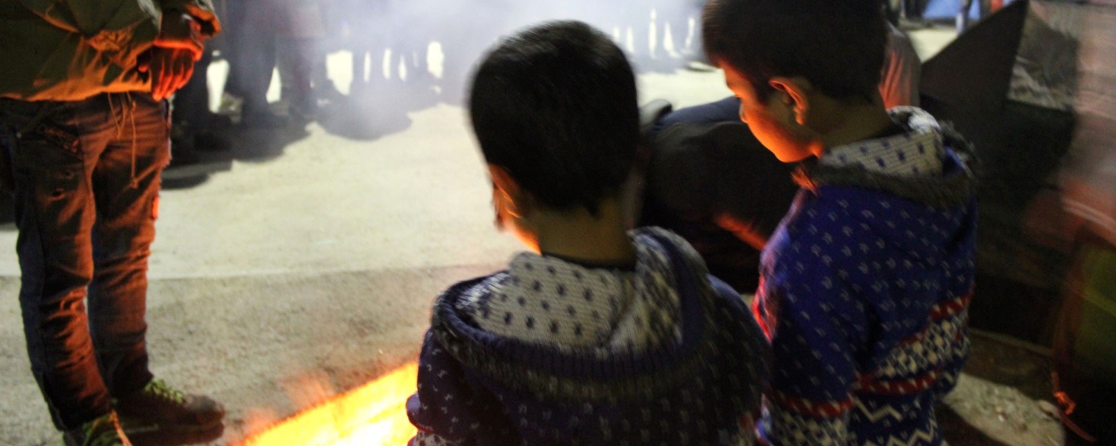 To små barn som befinner seg i Morialeiren varmer seg foran et bål