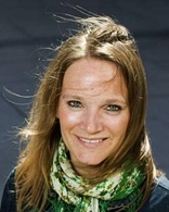 Portrett av smilende kvinne med grøndtspettet skjerf og vind som blåser i håret