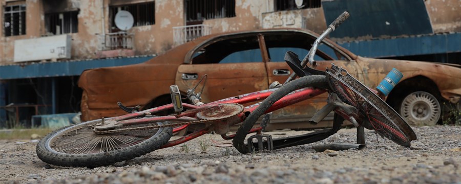 En sykkel og en utbrent bil ligger i en gate i Baiji, Irak, juni 2017. Foto: ICRC