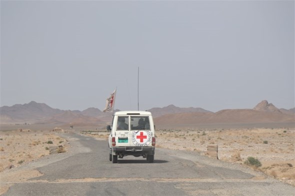EN bil med Røde Kors-logoer og et Røde Kors flagg på taket kjører i et øde landskap.
