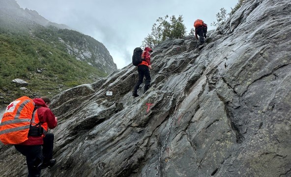 Tre frivillige fra Røde Kors klatrer oppover en bratt fjellside med hjelp av tau.
