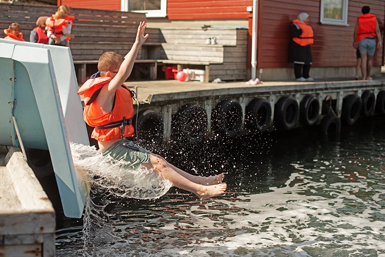 En gutt kommer ut fra en vannsklie med armene i været.