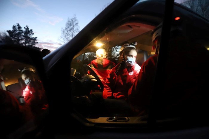 To personer med hvite hjelmer og Røde Kors uniform sitter i en varebil