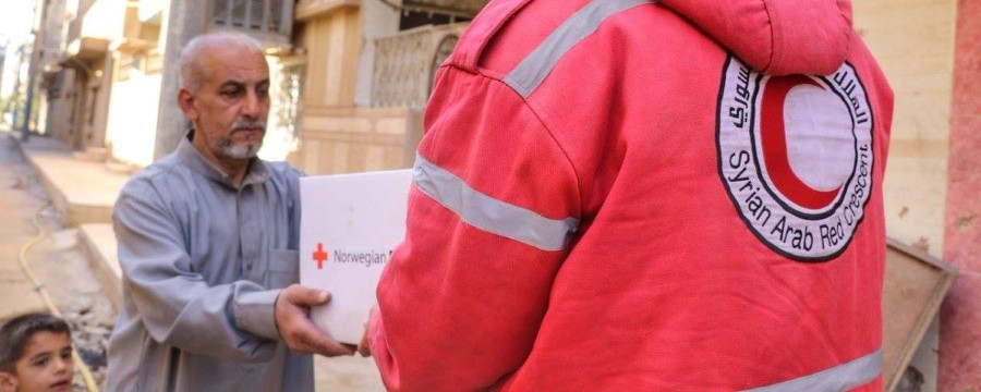 En eldre mann tar i mot en eske med nødhjelp fra frivillig i rød jakke